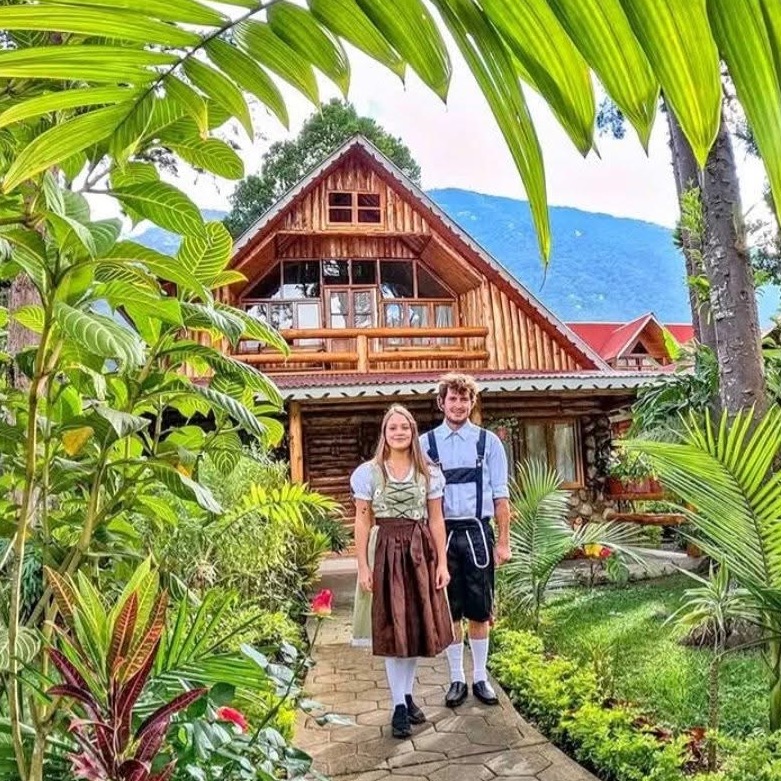 Holzhaus im alpenländischen Stil in Pozuzo, Frau in Dirndl und Mann in Trachtenlederhose