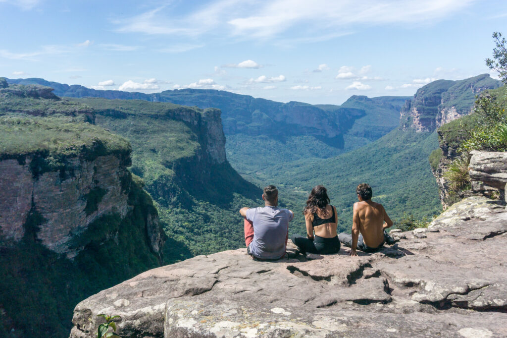 Drei Personen sitzen auf einem Aussichtspunkt und blicken über das Vale do Pati in der Chapada Diamantina in Bahia, Brasilien.