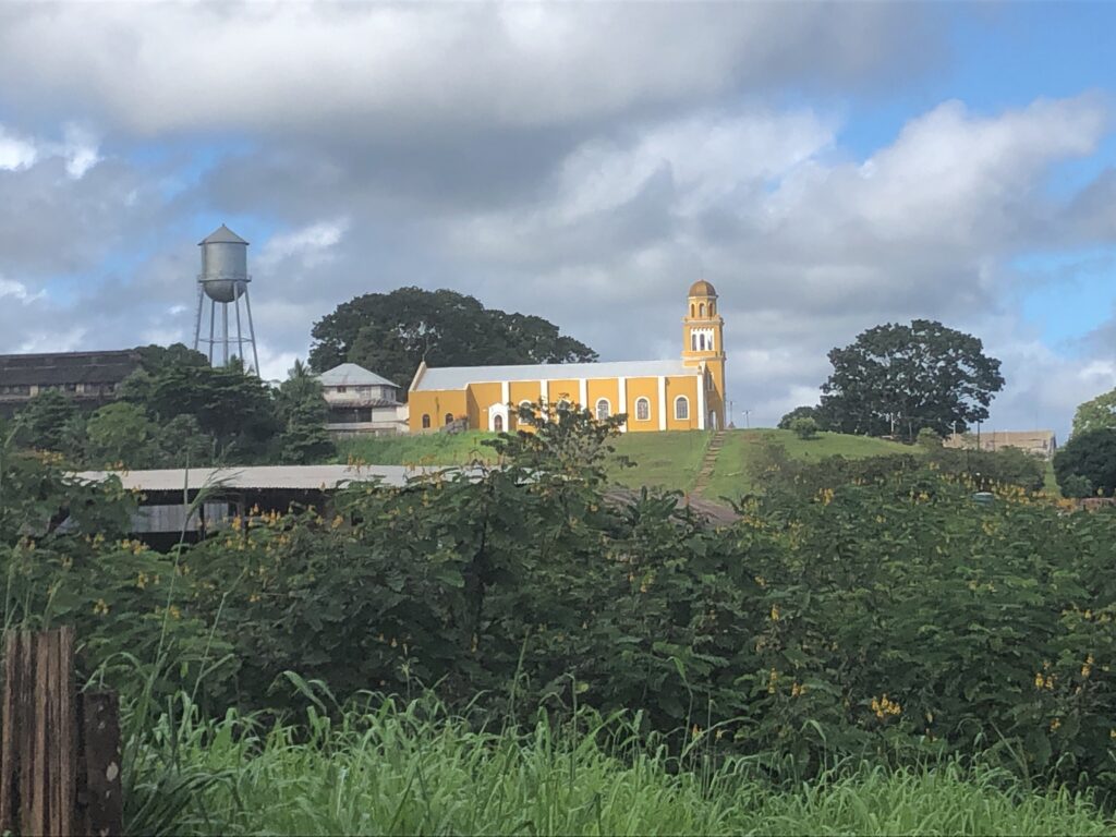 Gelbe Kirche auf einem Hügel in Fordlândia im brasilianischen Amazonasgebiet, dahinter ein amerikanischer Wasserturm.