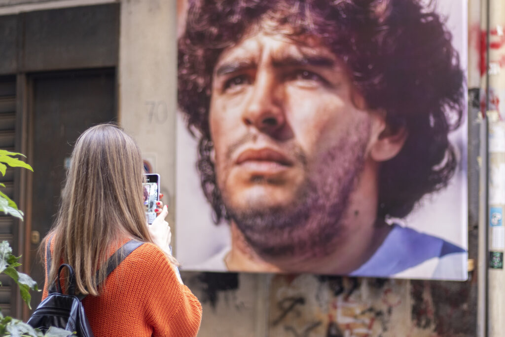 Frau steht vor einem Wandgemälde von Diego Maradona in Neapel